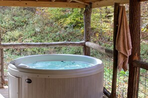A hot tub in a wooden deck area with a view of a wooded landscape.