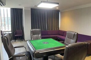 A room with a pool table, leather chairs, a purple sofa, and a small table with chairs.