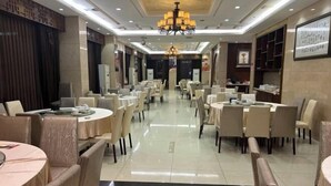 Um restaurante espaçoso com várias mesas e cadeiras redondas, um candelabro e um chão limpo revestido de azulejos.