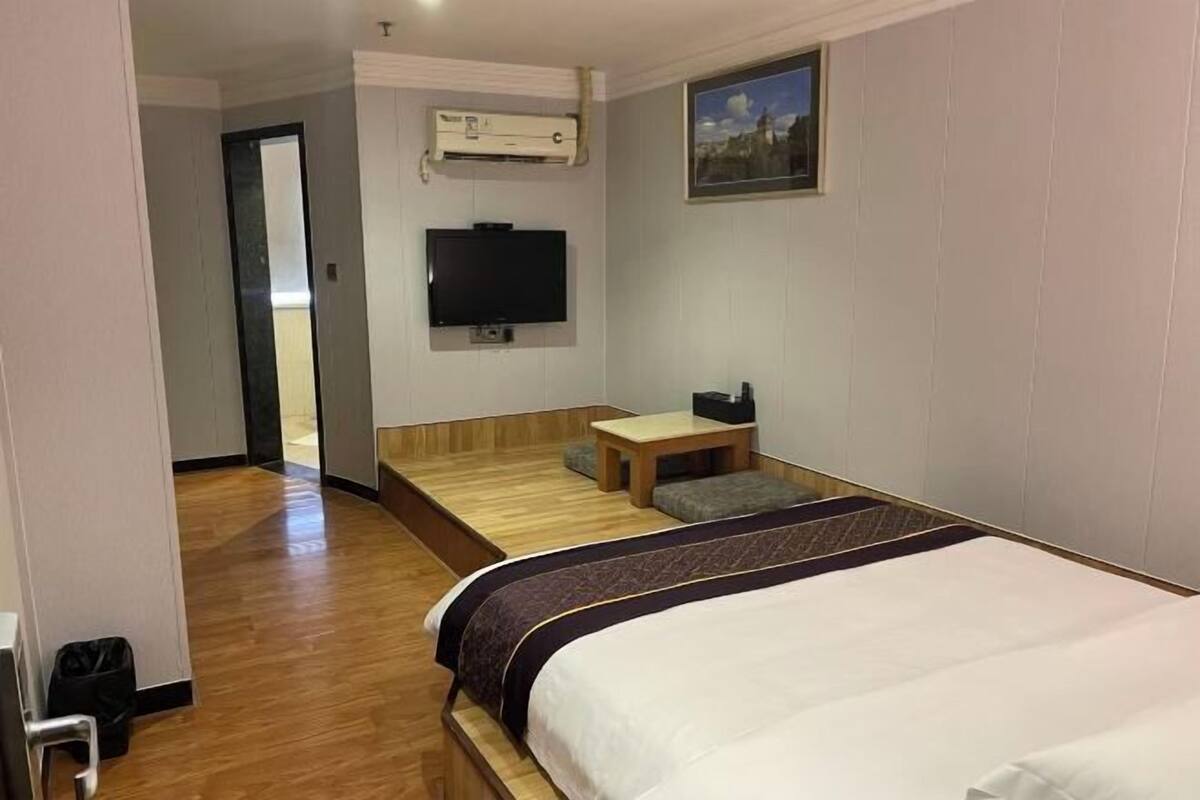 A hotel room with a bed, a small desk, a television, and an air conditioning unit.