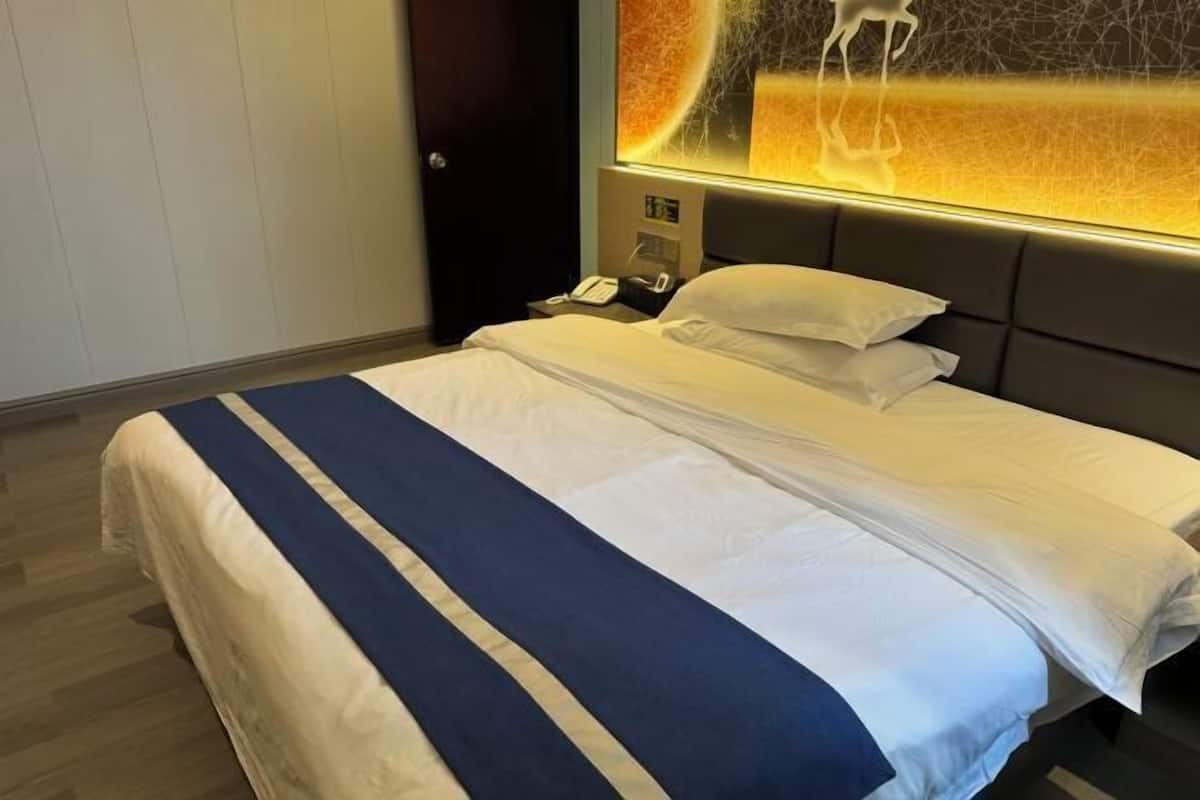 A hotel room with a bed, a nightstand, a phone, and a wall with a decorative light.