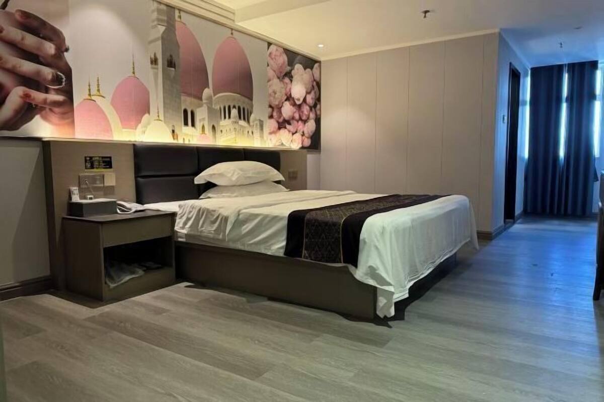 A modern hotel room with a large bed, bedside tables, a nightstand, a wall-mounted TV, and a large mirror.