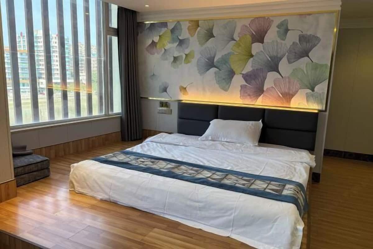 A modern hotel room with a large bed, a wall-mounted light fixture, and a view of buildings outside.