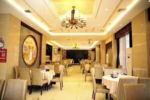 Zona de dinar d'hotel amb diverses taules i cadires, un candelabrum i un ampli quadre mural.