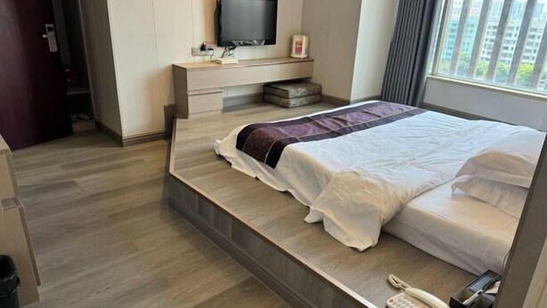 Quarto de hotel com cama, televisão, telefone e janela com vista.
