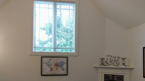A room with a high ceiling, a large window, a fireplace, two armchairs, a small table, and a framed map on the wall. - Brand New Cottage In Great Berkeley Neighborhood.  (Berkeley)