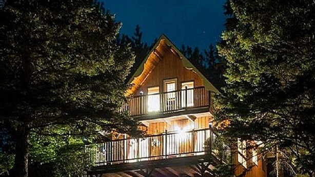 Une maison à deux étages dotée d’un balcon, entourée d’arbres et d’une pelouse bien entretenue.