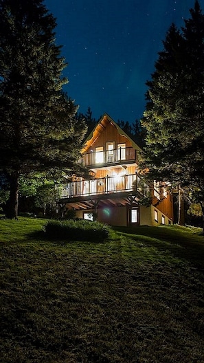 A two-story house with a balcony, surrounded by trees and a well-maintained lawn.