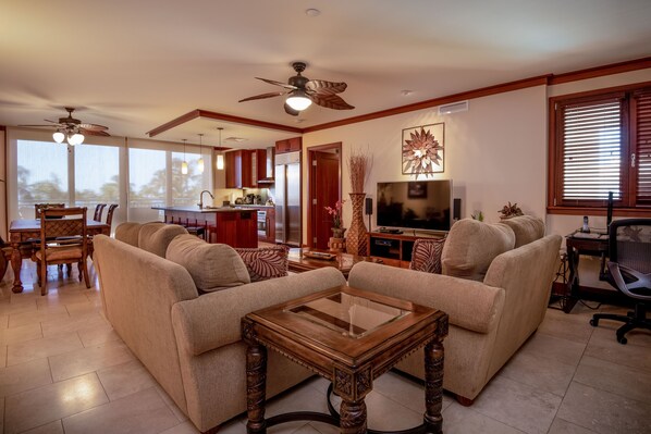 A spacious living room with a sofa set, a wooden coffee table, a television, and a dining area with a table and chairs.