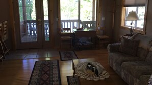 Ein Wohnzimmer mit einer Couch, einem Couchtisch mit einer Spitzeneinlage, Holzboden und Blick ins Freie durch eine Tür.