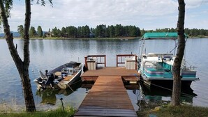 Eine Holzstege, der sich ins ruhige Wasser erstreckt, mit einem Boot an der rechten und einem kleineren Boot an der linken Seite.