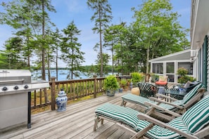 Een houten terras met een barbecue, lounge stoelen en potplanten.