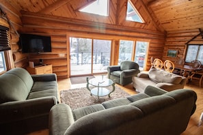 Ein gemütliches Blockhaus-Interieur mit einem großen Fernseher, bequemen Sitzmöglichkeiten und Blick ins Freie.