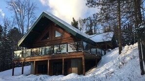 Une cabane en bois dotée d’un grand balcon et d’un toit à forte pente, entourée de neige et d’arbres.
