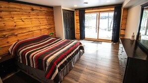 Une chambre avec un mur en bois, un lit recouvert d’une courtepointe à rayures, une commode et une porte-fenêtre coulissante donnant sur un balcon.