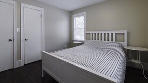 A bedroom with a white bed, a window with blinds, a white door, and a small white table. - JUST REMODELED top to bottom -  master bed/bath on main floor! (Cleveland Heights)