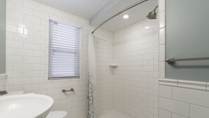 A bathroom with white tiles, a toilet, a sink, a shower with a glass door, and a window with blinds. - JUST REMODELED top to bottom -  master bed/bath on main floor! (Cleveland Heights)