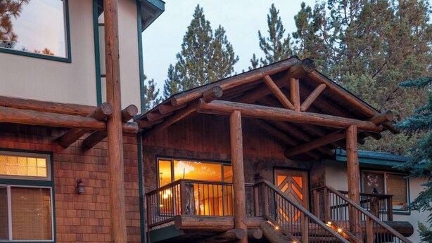 Une cabane en rondins dotée d’une terrasse en bois et d’un escalier menant à un porche.