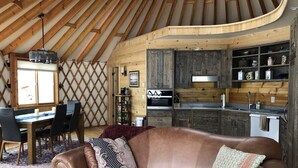 A cozy interior with a wooden ceiling, a leather sofa, a dining area, and a kitchen with wooden cabinets. - Luxury Yurt bordering Flathead Lake (Somers)