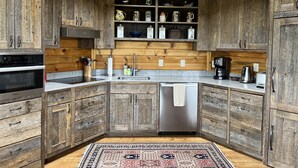A rustic kitchen with wooden cabinets, a stainless steel dishwasher, and a variety of kitchenware on shelves. - Luxury Yurt bordering Flathead Lake (Somers)