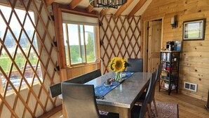 A wooden interior with a dining table, chairs, a bookshelf, and a large window with a view. - Luxury Yurt bordering Flathead Lake (Somers)