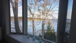 Huoneessa on suuri ikkuna, josta avautuu näkymä järvelle, sekä puulattia ja ikkunalaudalla kolme lasista kynttilänjalkaa.