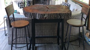 Un espacio de estar al aire libre con techo, una chimenea de piedra y muebles de mimbre. Encima de la chimenea, hay un televisor.