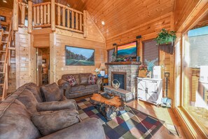 A log cabin interior with a wooden staircase, a fireplace, a sofa, and a large window. - Top of Beautiful Legacy Mountain Resort, Amazing Views, Game Room 2 king suites (Sevierville)