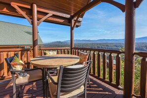 Une terrasse en bois avec une table ronde et des chaises, offrant une vue sur un paysage montagneux.