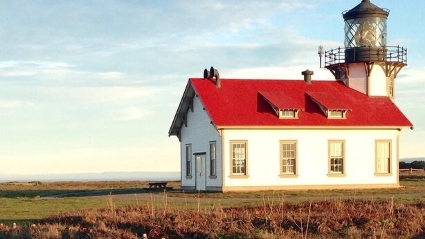 Un phare avec un toit rouge et un bâtiment blanc à côté.