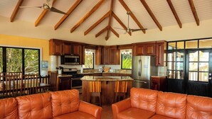 A spacious kitchen with wooden cabinets, a central island, and a dining area with leather sofas. - Large 5+ Bedroom Oceanfront w/ Pier and Pool (Placencia)