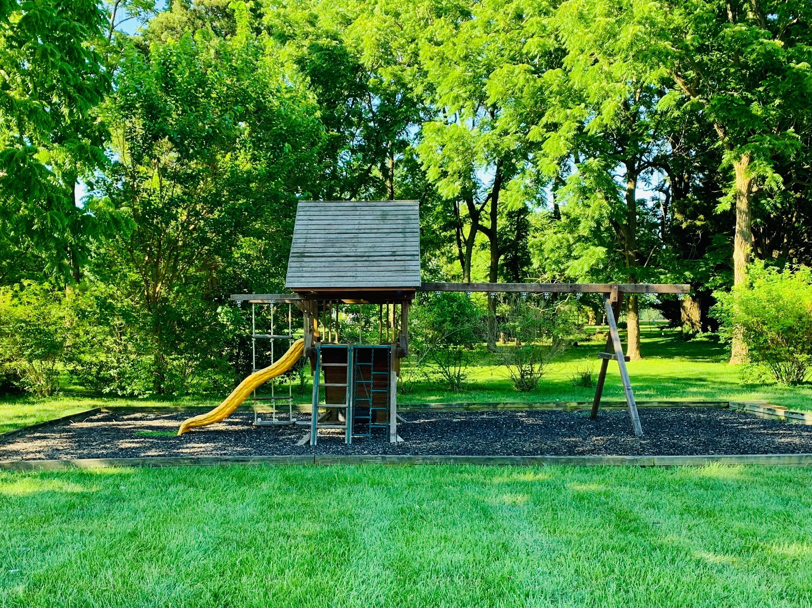 A playground with a wooden playhouse, a yellow slide, and swings.