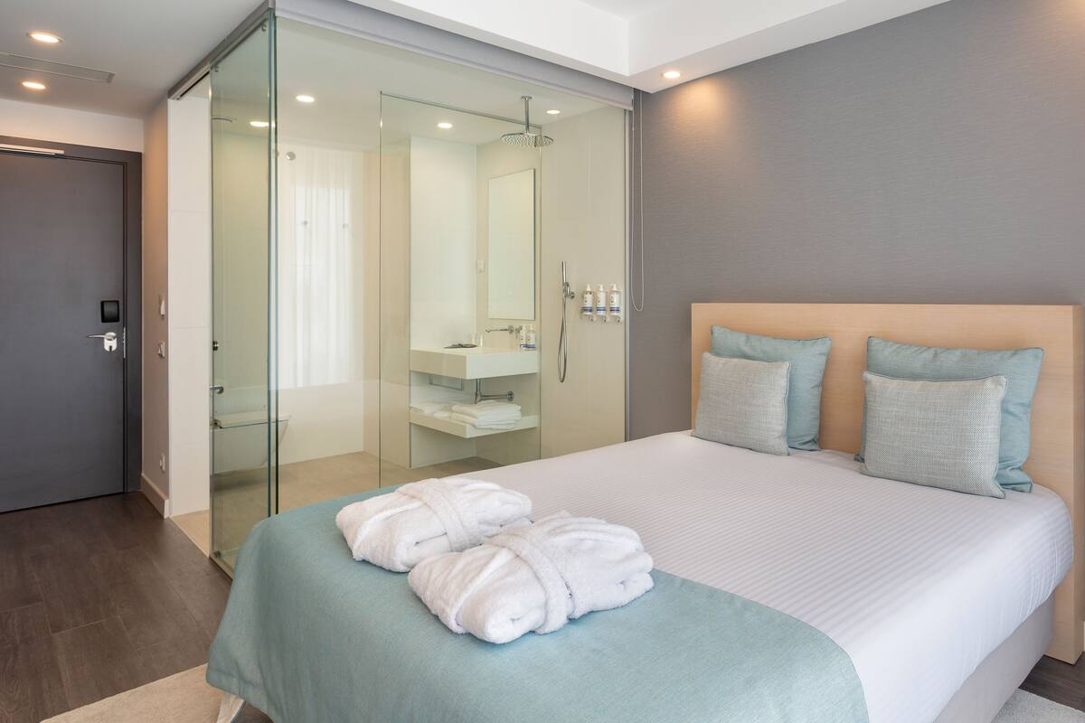 A modern hotel room with a large bed, two pillows, a glass shower enclosure, and a visible bathroom.
