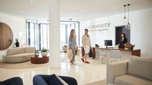 A modern hotel lobby with a reception desk, seating area, and large windows. - Longevity Health and Wellness Hotel - Adults Only (Portimão)