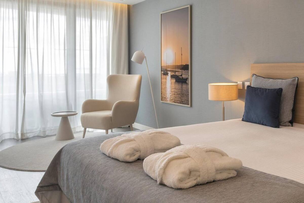 A hotel room with a bed, a chair, a lamp, and a painting on the wall.