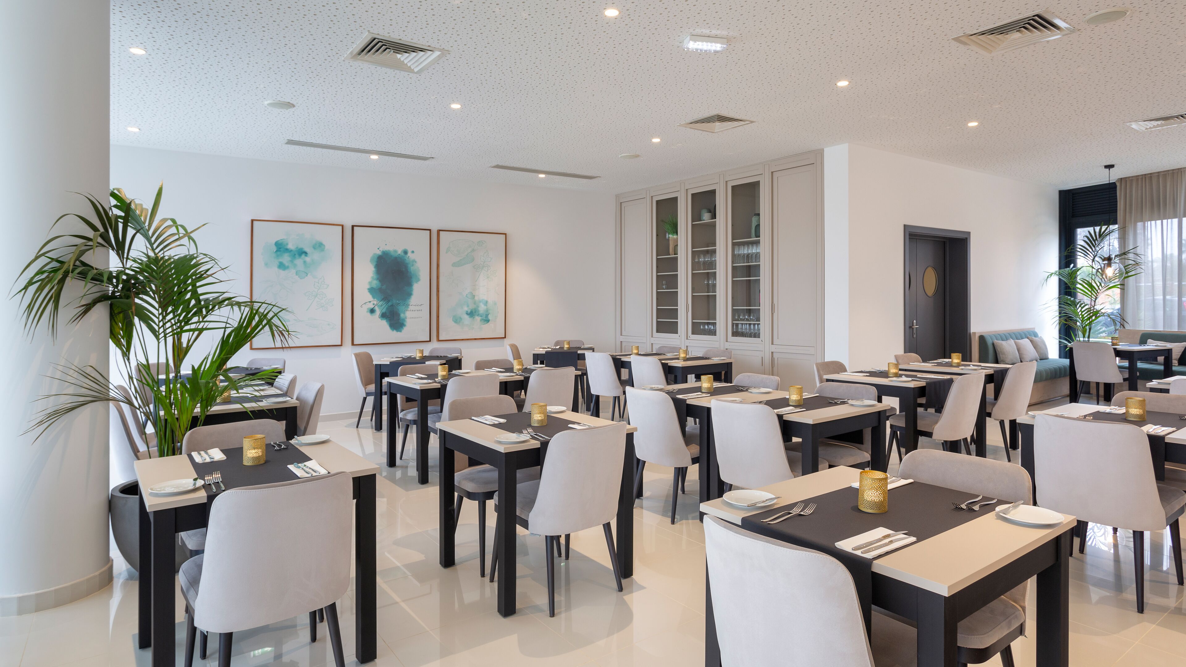 Een moderne eetruimte met tafels en stoelen, grote ramen en kunst aan de wanden.