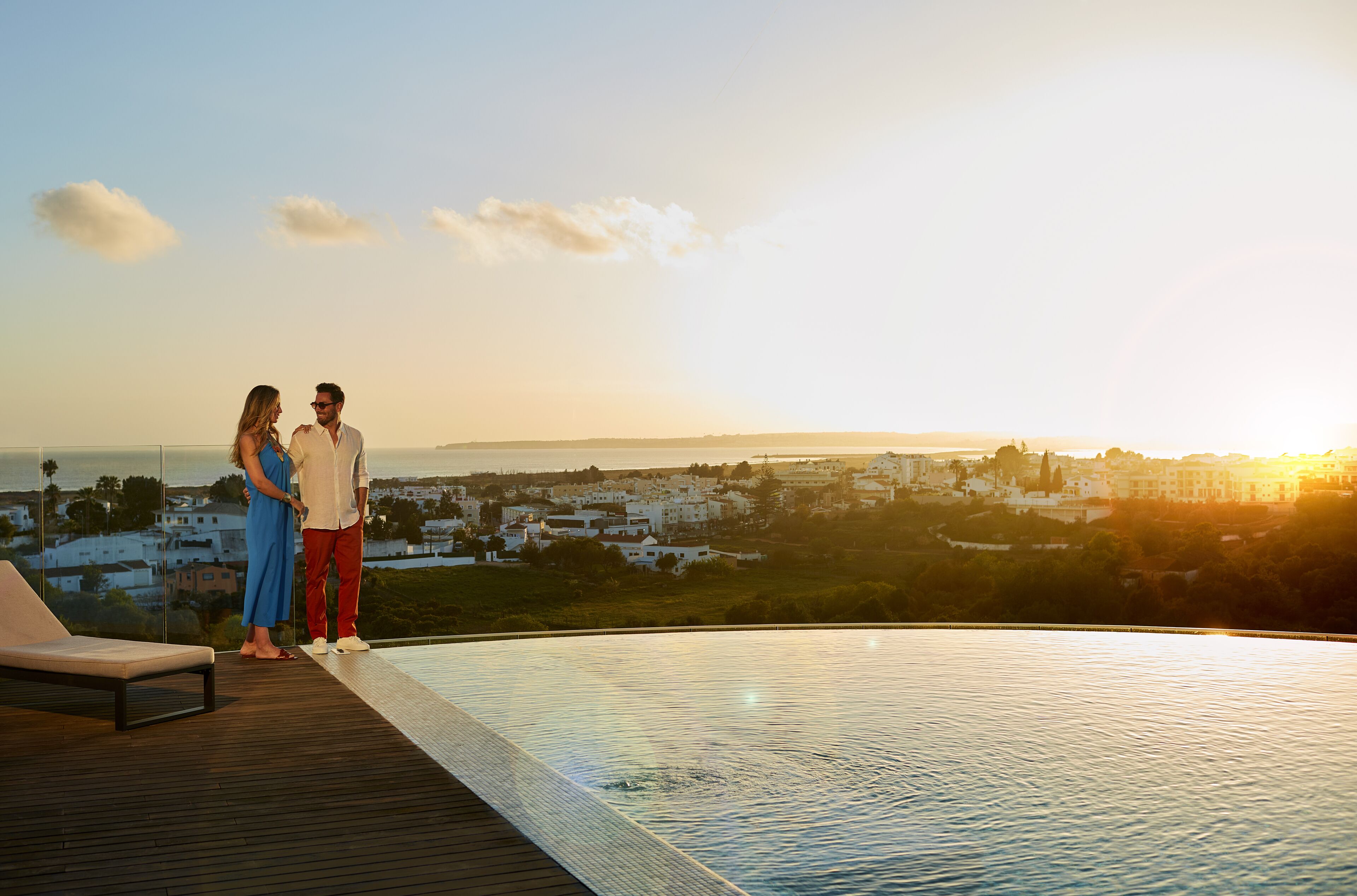 A couple standing on a deck overlooking a cityscape at sunset.