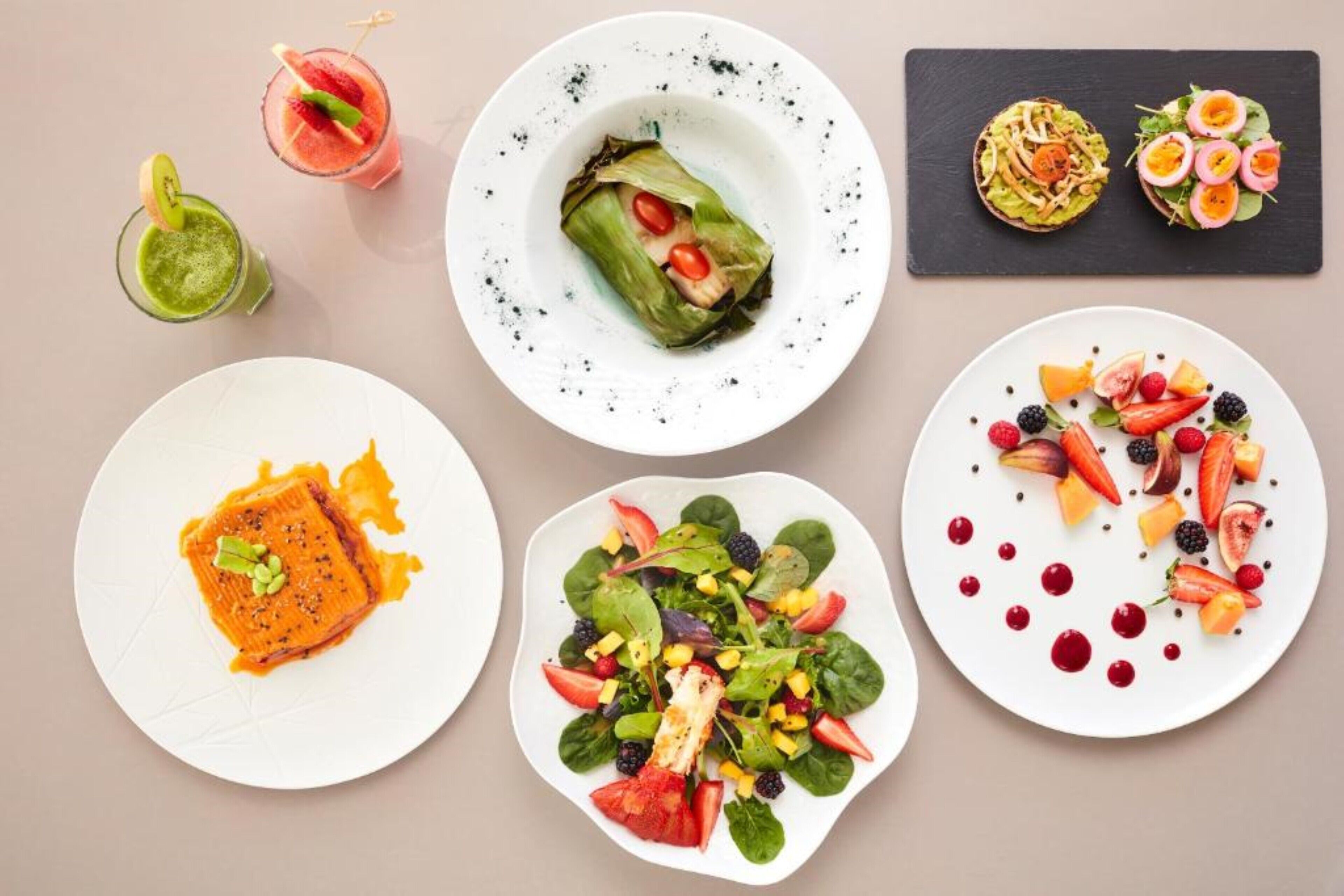 Variedad de platos, incluyendo un plato de salmón, una ensalada y dos bebidas a base de fruta.