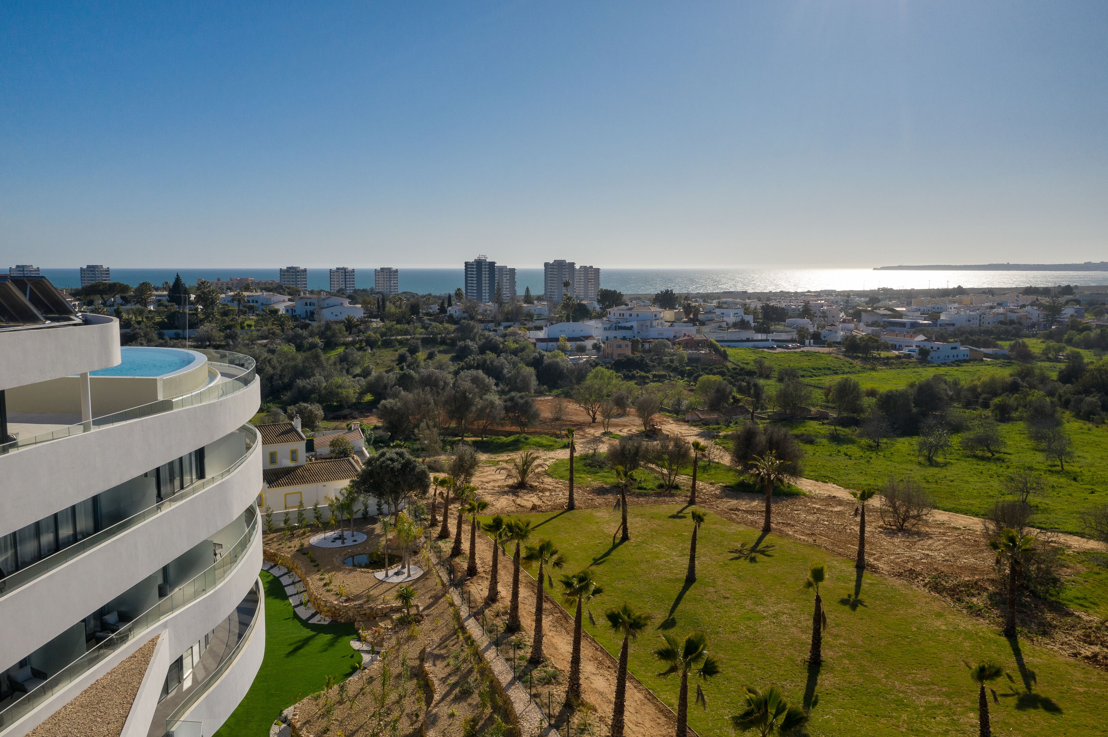 Un edificio moderno con un balcón curvo que da a una zona costera con vegetación y vistas al mar.