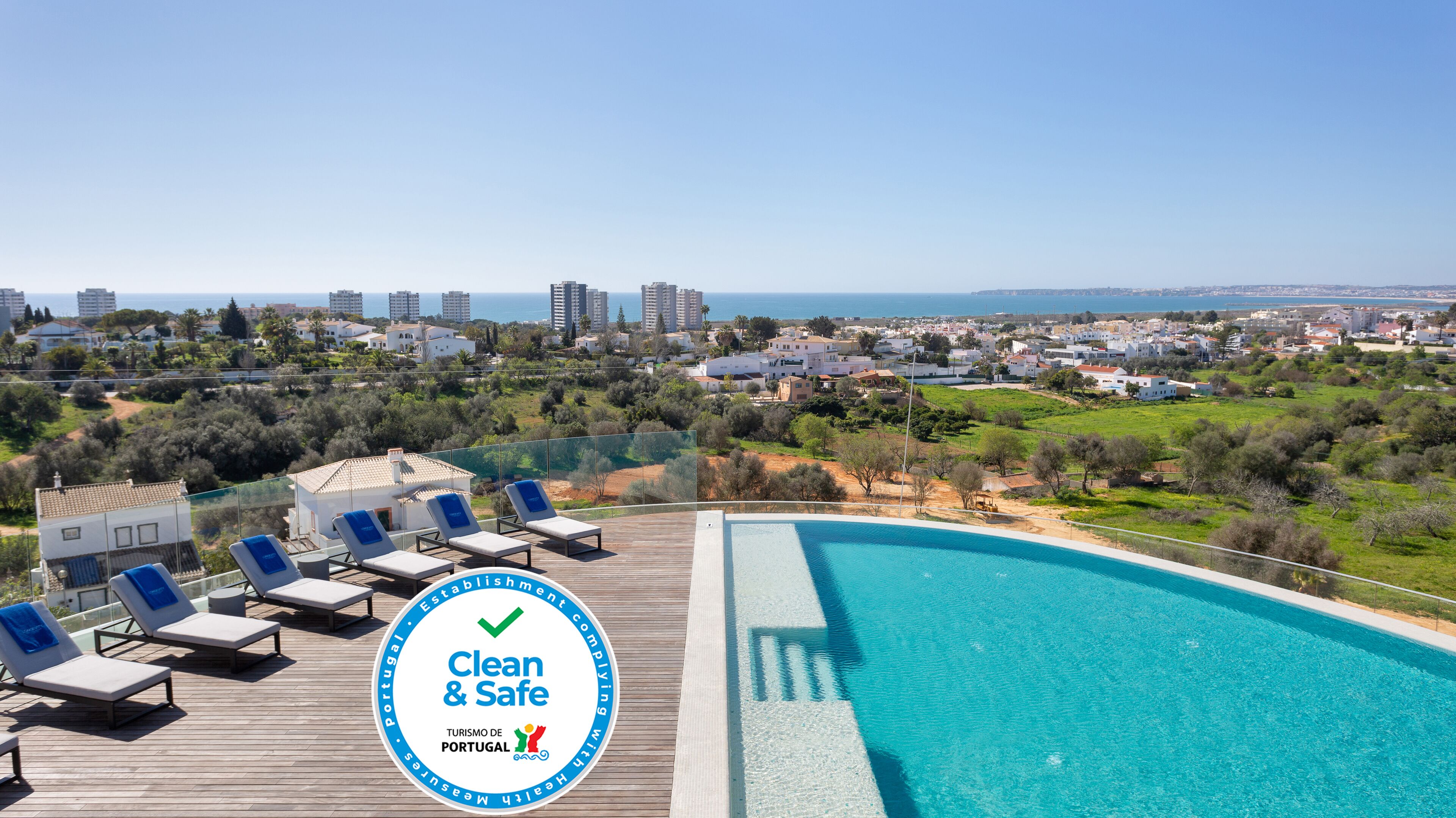 A pool area with lounge chairs, a clear view of the sea, and a "Clean & Safe" sign.