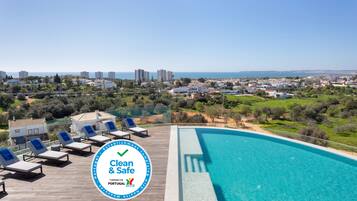 A pool area with lounge chairs, a clear view of the sea, and a "Clean & Safe" sign.