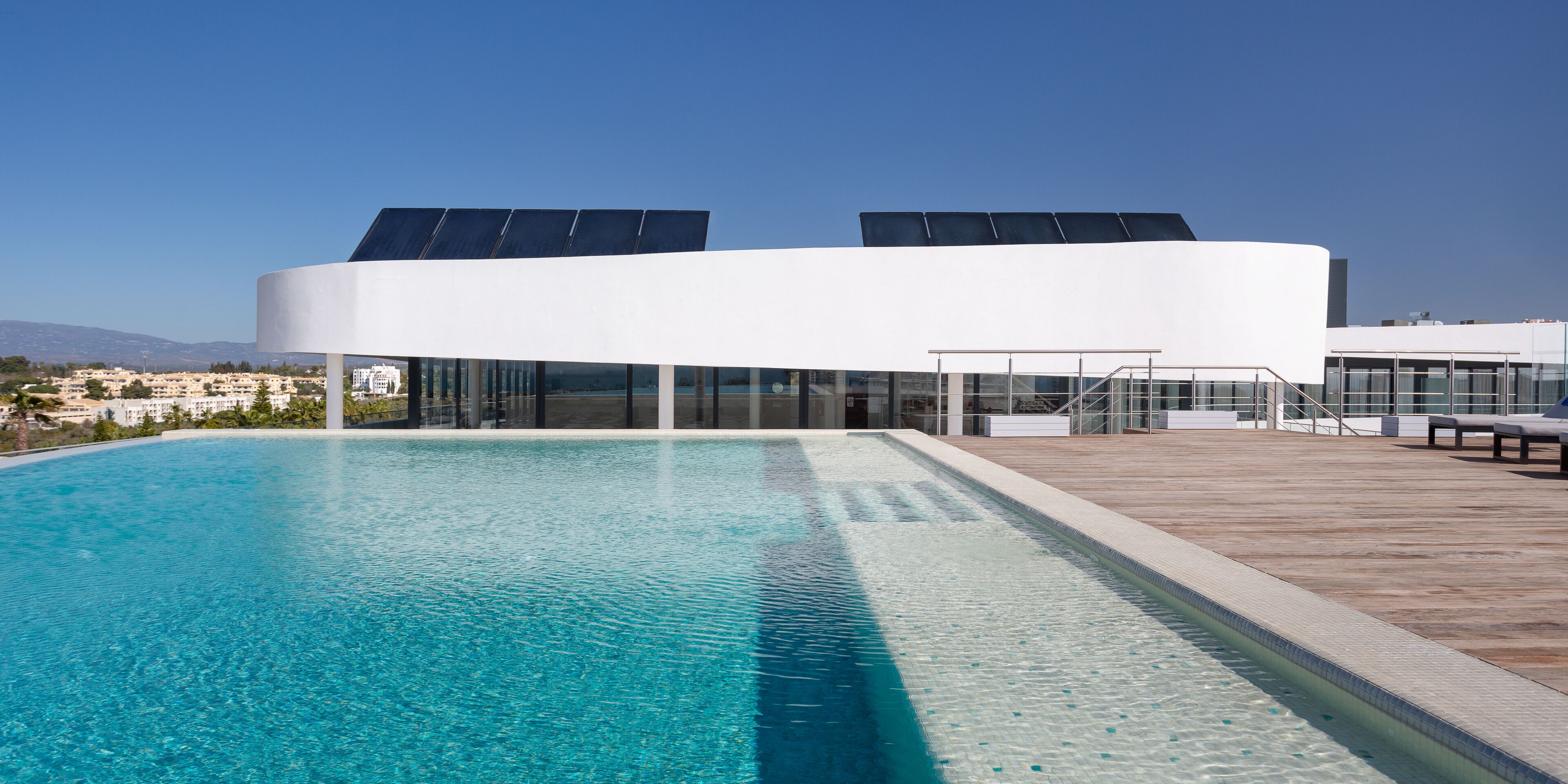 A modern building with a swimming pool, solar panels, and a wooden deck.