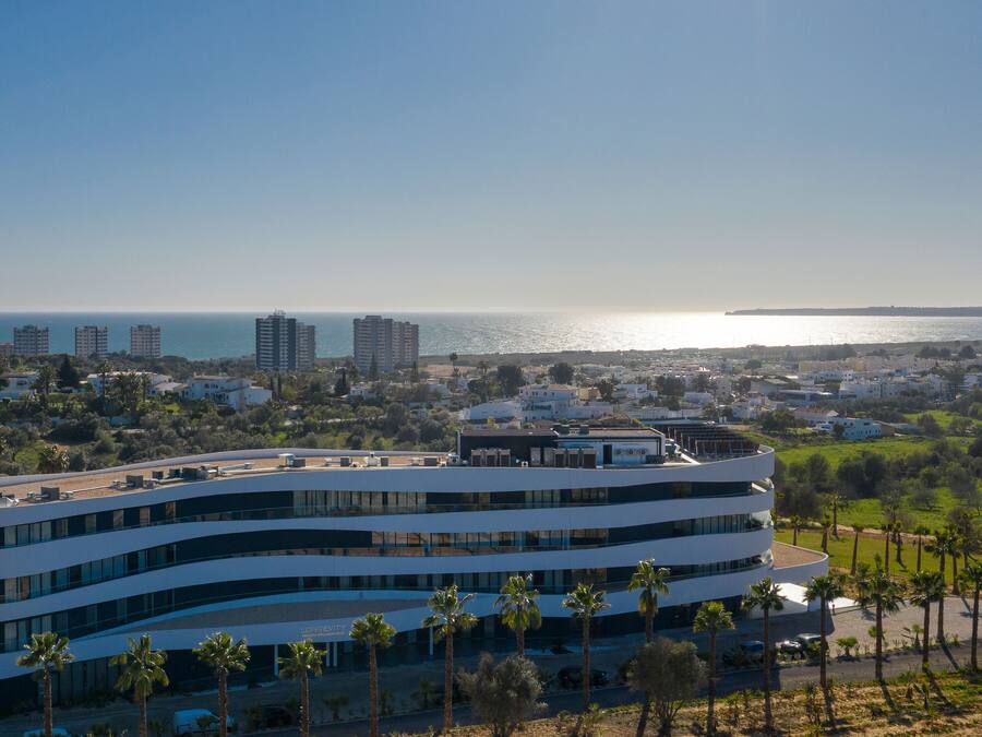 A modern hotel with a curved facade, multiple balconies, and a view of the sea.