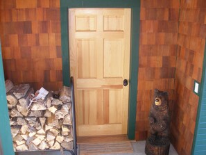 A wooden door with a green trim, a bear statue, and a stack of firewood.