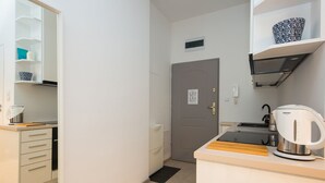 A compact kitchen with a coffee maker, a kettle, and a microwave. There is a door with a sign above it and a shelf with a decorative bowl. - ShortStayPoland Środkowa (B48) (Warsaw)