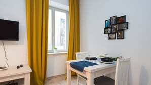 A dining area with a table set for two, a television on the wall, and a window with yellow curtains. - ShortStayPoland Środkowa (B48) (Warsaw)