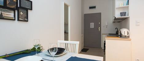Quarto compacto com uma mesa de jantar para dois, cozinha compacta e porta que dá acesso a outro espaço.