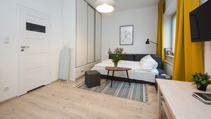 A modern, well-lit room with a bed, a small table, a sofa, and a TV mounted on the wall. - ShortStayPoland Środkowa (B48) (Warsaw)