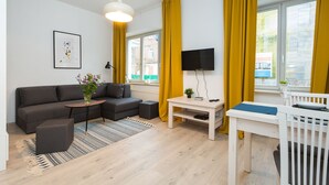 A modern living room with a sofa, coffee table, and dining area, featuring a large window with curtains. - ShortStayPoland Środkowa (B48) (Warsaw)