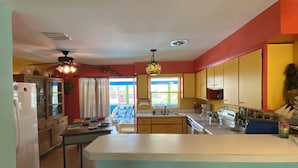A kitchen with a central island, wooden stools, a refrigerator, and a dining area with a table and chairs.